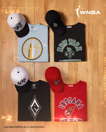COLLECTION OF SPORTS-THEMED T-SHIRTS AND CAPS ON A WOODEN SURFACE WITH WNBA BRANDING.